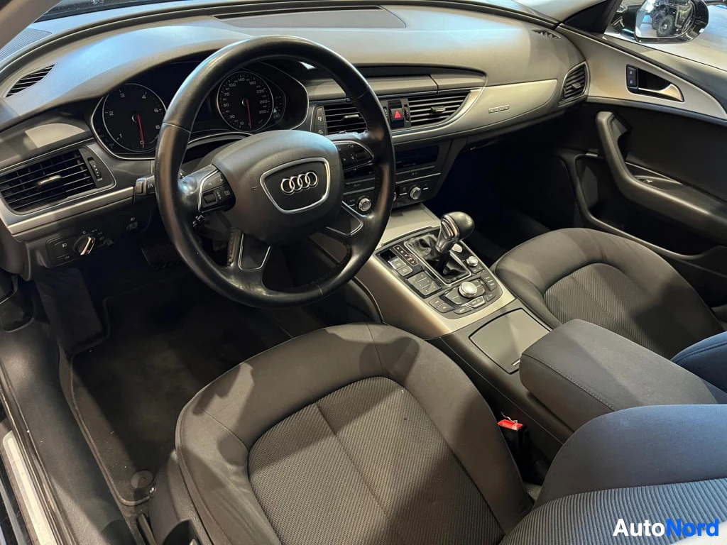 Muu: Audi A6:n ohjaamo kuljettajan puolelta: monitoimiohjauspyörä, kojelauta, vaihteenvalitsin ja keskikonsoli, tummat kankaanverhoillut istuimet.