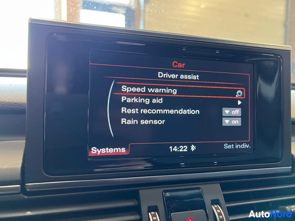 Yksityiskohta: Audi A6:n keskinäyttö näyttää Driver assist -valikon, jossa on Speed warning, Parking aid, Rest recommendation ja päällä oleva Rain sensor.
