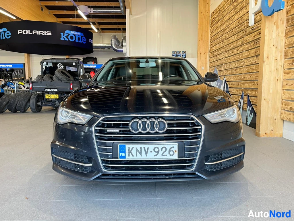 Edestä: Mustan sedanin etukuva; etusäleikkö Audi-merkeillä, ajovalot ja rekisterikilpi.