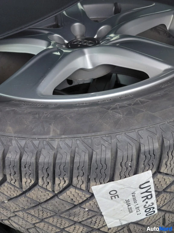 Yksityiskohta: Ajon viileä rengas taka- tai varapyörässä, hopeanvärisellä Audi-vanneteollaan; renkaassa valkoinen varastotarrateksti.