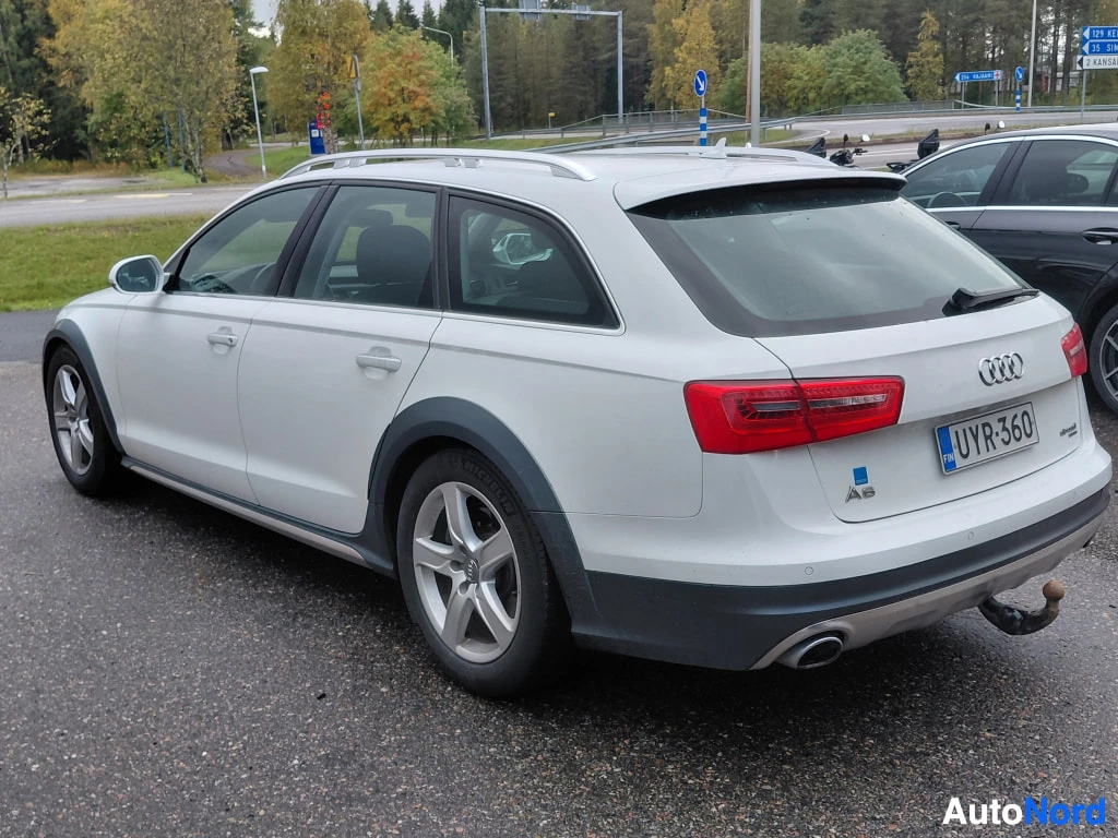 Takaviisto: Auton takaosa ja vasen sivu valkoisesta farmarista: takaosaan päin käännetty kulma, -kilpi, A6-merkki, Audi-renkaat ja hopeiset vanteet.