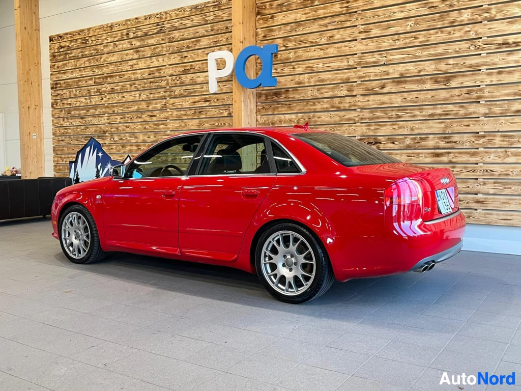 Takaviisto: Punainen Audi S4 -sedan taka­kulmasta sisätiloissa, neljä pakoputkea ja viisto takalasi näkyvät.