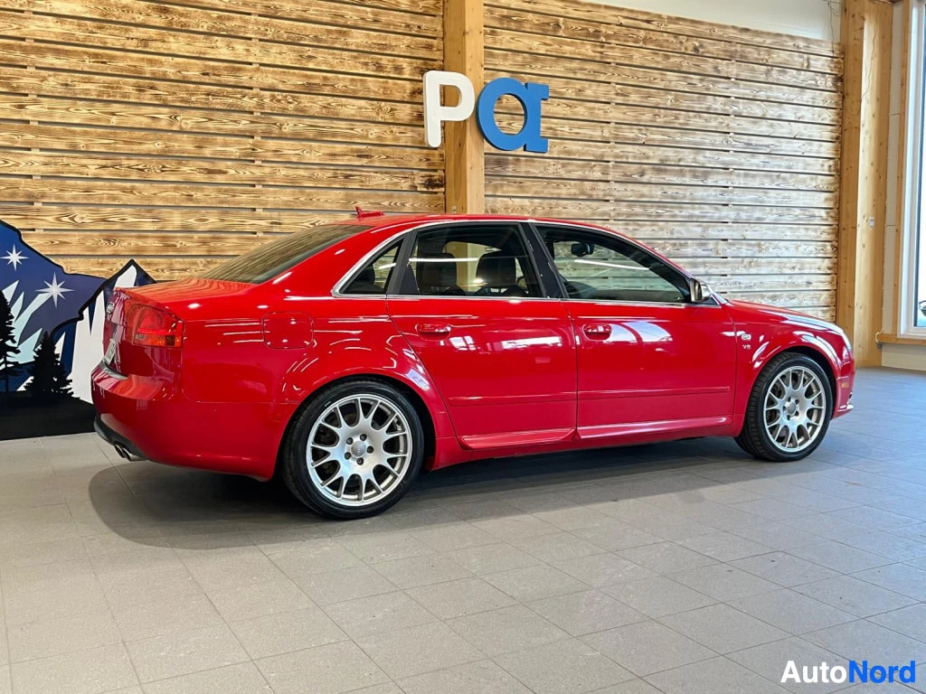 Takaviisto: Punainen sedan Henkilöauto takaviistosta kuvattuna sisätiloissa.