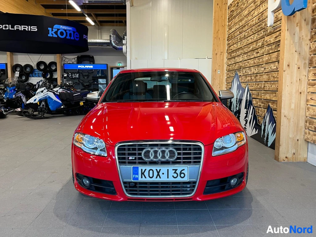 Edestä: Punainen sedan Henkilöauto edestä kuvattuna sisätiloissa, rekisterikilpi.
