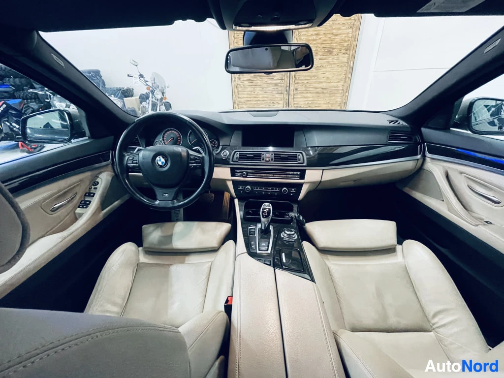 Muu: Auton sisätilat etupenkiltä kuvattuna: BMW-ohjauspyörä, beige-punainen kojelauta, kaksivärinen sisusta ja keskikonsoli näkyvät.