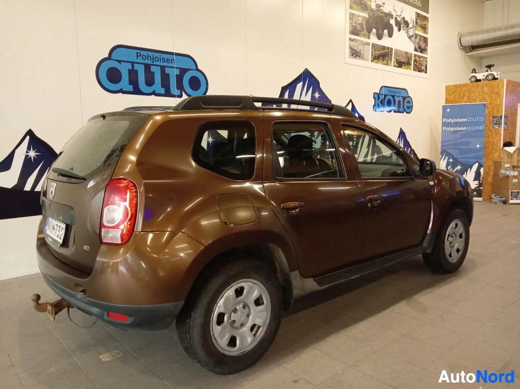 Takaviisto: Ruskea Dacia Duster takaa- ja sivulta kuvattuna sisätiloissa, takavalot ja rekisterikilpi näkyvissä.