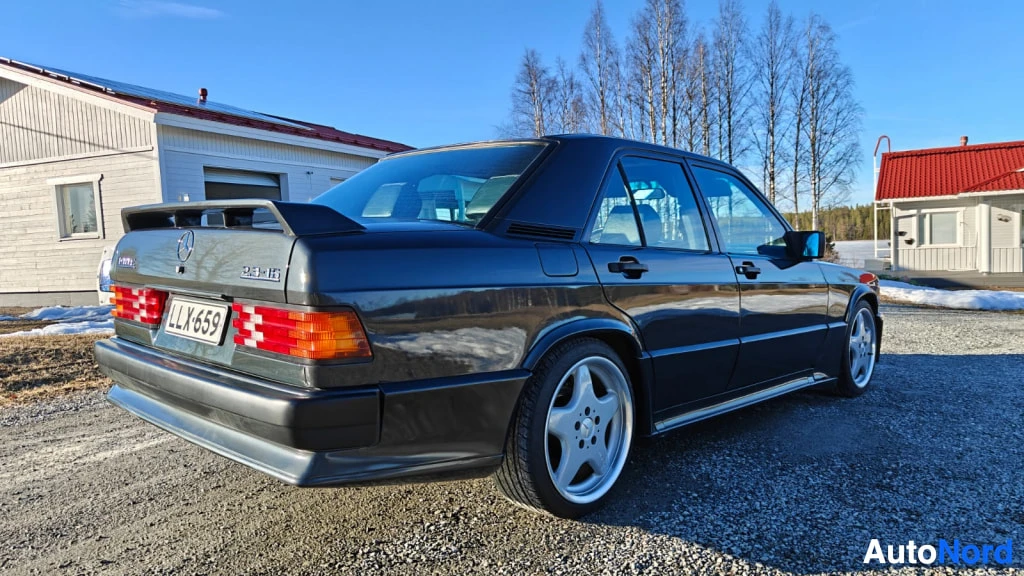 Takaviisto: Aurinkoinen ulkokuvat takaa ja oikealta kyljestä: tumma Mercedes-sedan ilmassa, rekisterikilpi LL X659.