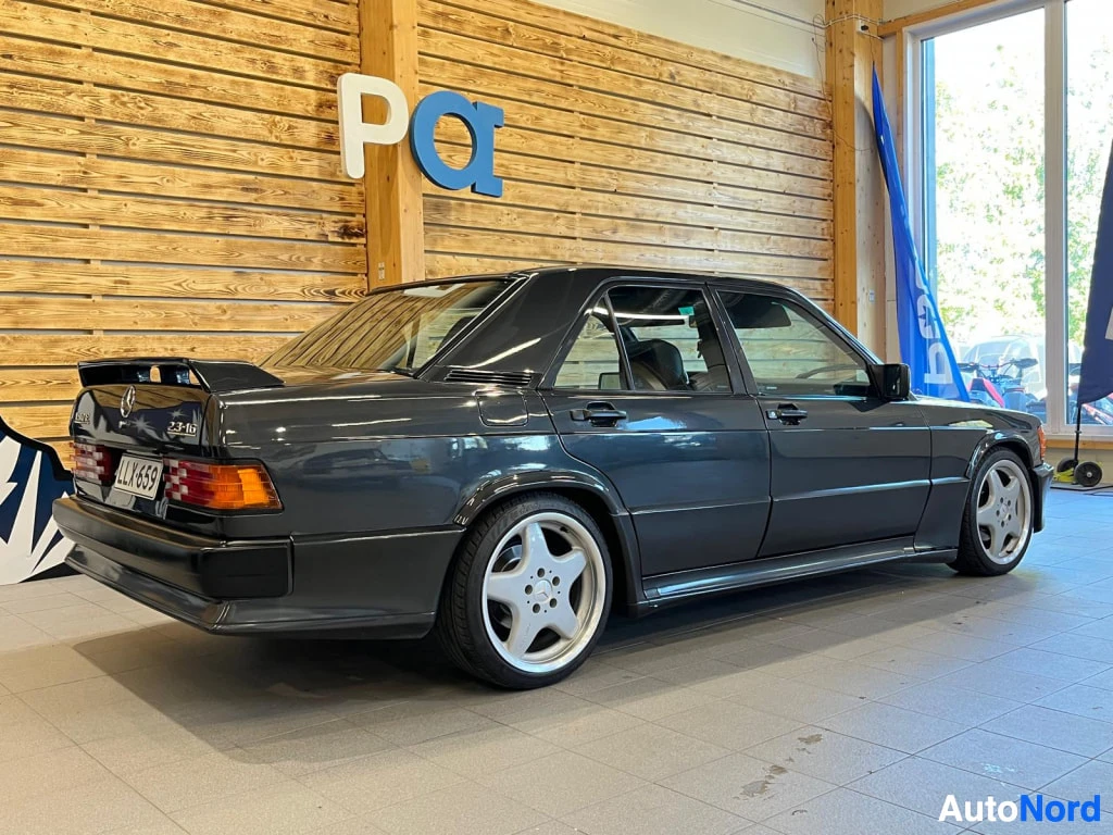 Takaviisto: Mercedes-Benz 190 sedan takaviisto oikealta, tummanharmaa kori, spoileri takaluukussa ja viisipiiset kevytmetallivanteet, rekisteritunnus.