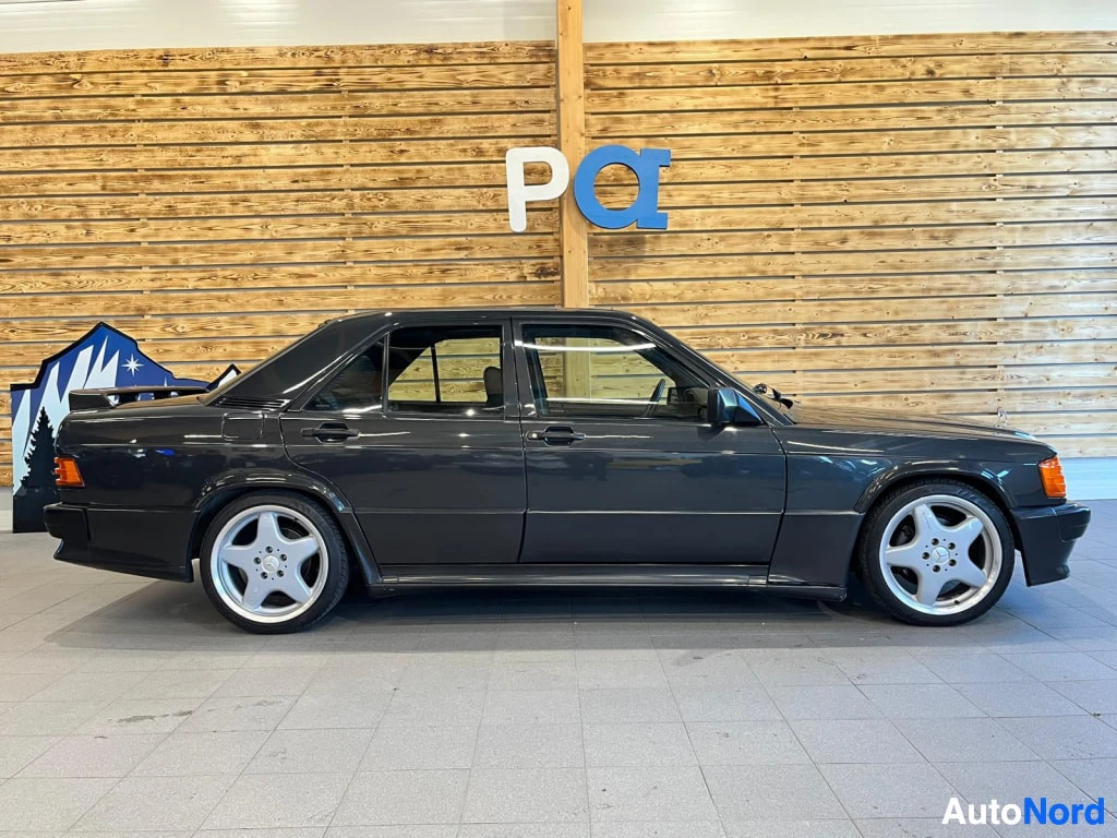 Sivulta: Mercedes-Benz 190 sedan sivukuva oikealta, tummanharmaa kori, viisipiiset kevytmetallivanteet ja ovista näkyvä tumma sisusta.