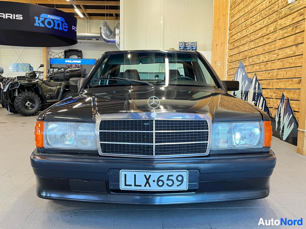 Edestä: Mercedes-Benz 190 sedan etukuva suoraan edestä, tummanharmaa kori, kromiläuvikko ja Mercedes-tähti konepellissä, rekisteritunnus.