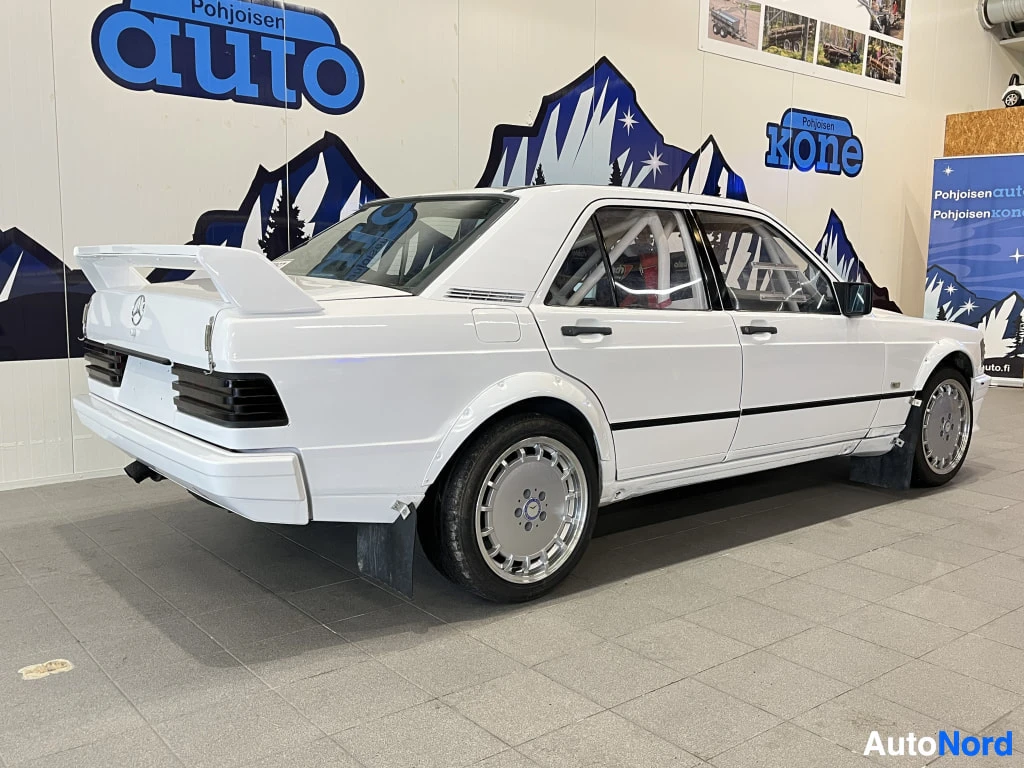 Takaviisto: Valkoinen Mercedes-Benz 190 -sedan takaa kulmasta kuvattuna suuren takasiiven kanssa sisätiloissa.
