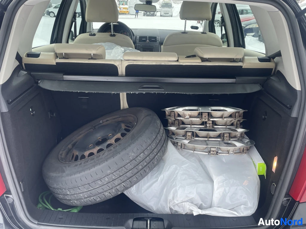 Tavaratila: Interior view of the cargo area behind the rear seats containing a spare wheel and a set of chrome rims stacked in plastic