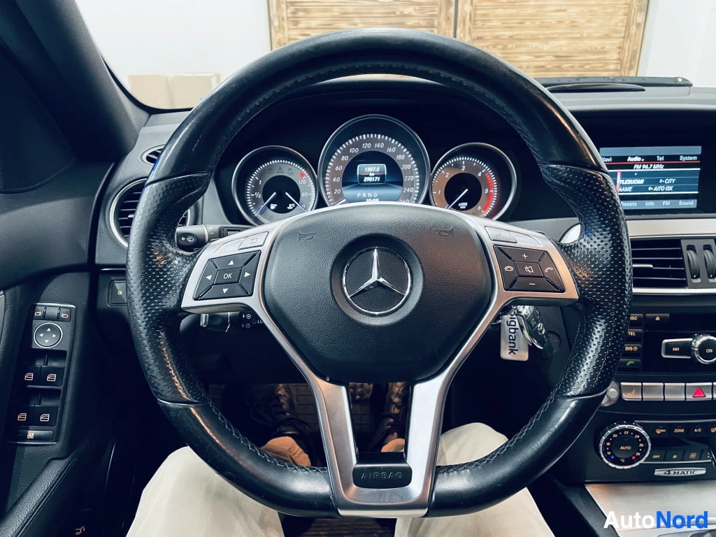 Sivulta: Ohjauspyörän lähikuva Mercedes-tähtimerkillä, mittaristot taustalla.