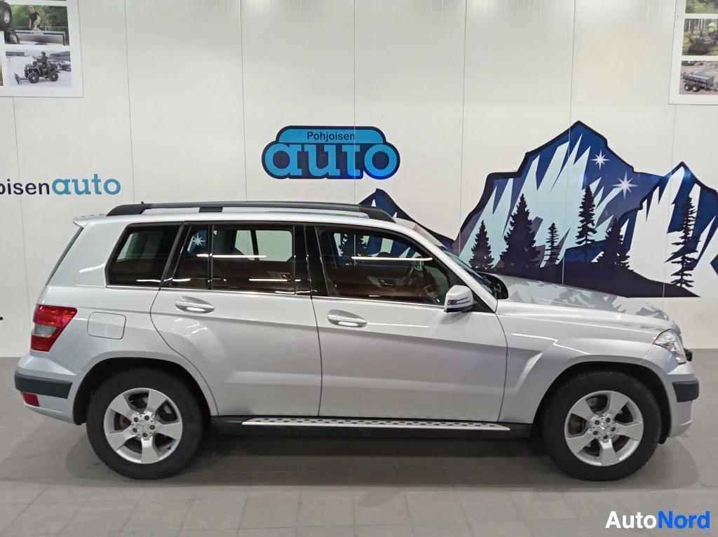 Sivulta: Profile view of a silver Mercedes-Benz GLK on display. Visible features include five-spoke alloy wheels, black roof rails, running boards along the lower body,