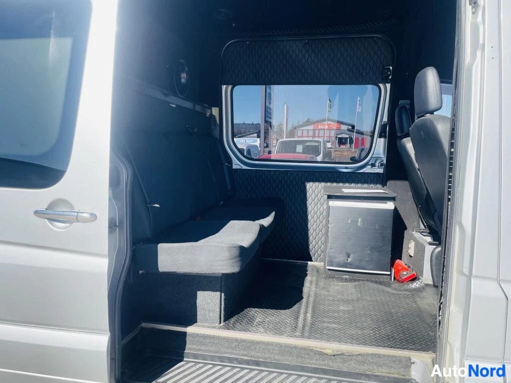 Muu: Mercedes-Benz Sprinterin takaosan sisätila avatusta takaovesta katsottuna: tumma penkki, timanttikuvioitu verhoilu, keittiöyksikkö ja palosammutto lattiassa.