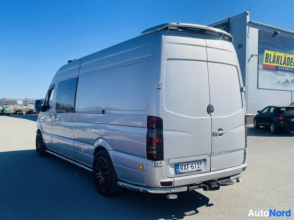 Takaviisto: Hopeanvärinen Mercedes-Benz Sprinter -pakettiauto takakulmasta, rekisteritunnus, kattoteline ja vetokoukku näkyvissä.