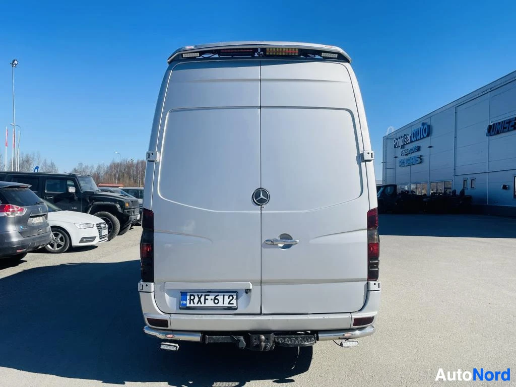 Takaa: Pakopäristyskuva hopeanharmaasta Mercedes-Benz Sprinter -pakettiautosta; takavalaistut takavalot, Mercedes-tähti ja rekisterikilpi, kattoreunassa lisävaloja.