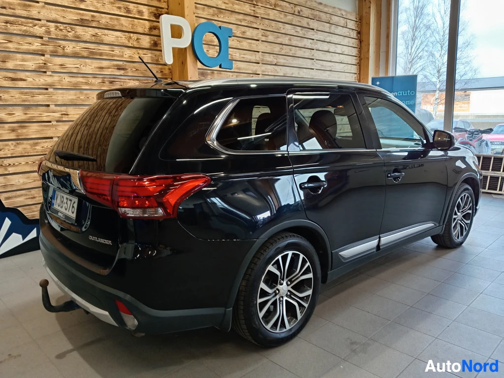 Takaviisto: Mustan Mitsubishi Outlander -maasturin takakulmanäkymä sisätiloissa; rekisteritunnus, takavalot ja hinauskoukku näkyvät.