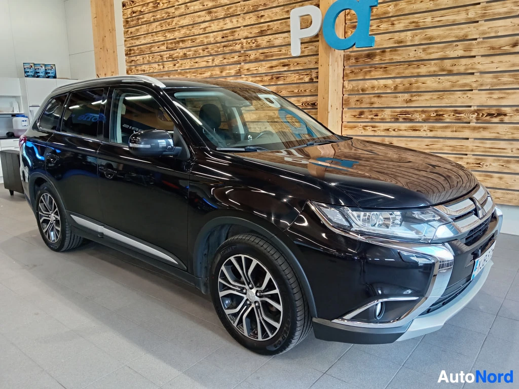 Etuviisto, nokka oikealle: Mustan Mitsubishi Outlanderin etukulmanäkymä showroomissa; kattotelineet ja harkotetut alumiinivanteet näkyvät.