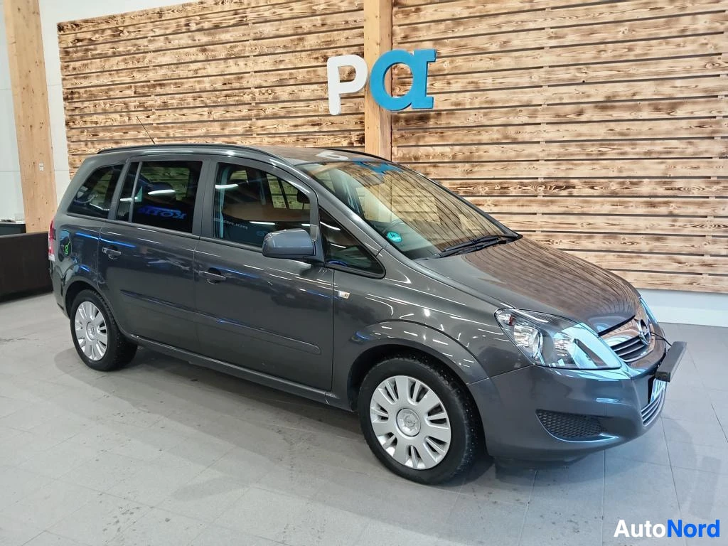 Etuviisto, nokka oikealle: Tummanharmaa Opel Zafira -tilavaunut näkyvissä sisätiloissa etukulmasta, kevytmetallivanteet ja kattokaiteet.
