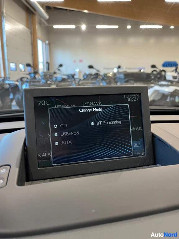 Yksityiskohta: Irrotettava infotainment-näyttö kojelaudassa näyttää äänilähteiden valinnan: CD, USB/iPod, AUX ja BT Streaming, taustalla navigointikartta ja kello 16:27.