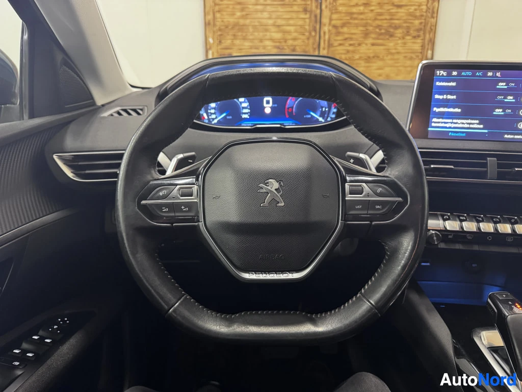 Muu: Ohjaamon näkymä Peugeot-merkkisestä autosta: ohjauspyörä, digitaalinen mittaristo ja kosketusnäyttö, jossa on auton asetusvalikko suomeksi.