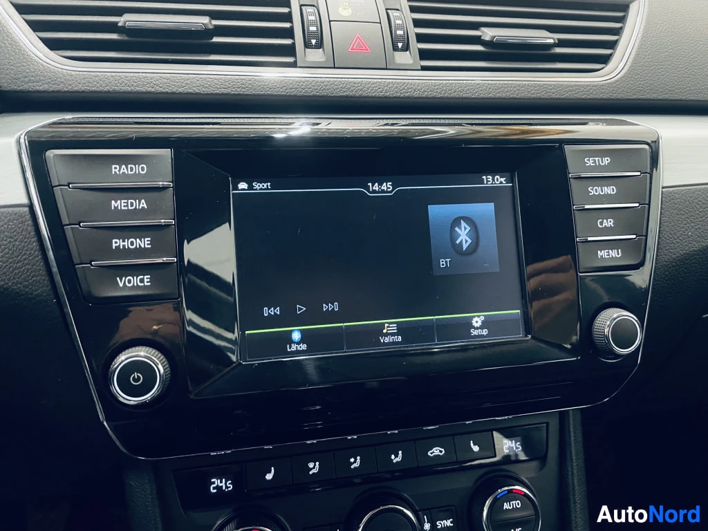 Yksityiskohta: Keskikonsolin lähikuva: infotainment-näyttö, jossa Bluetooth-symboli (BT), kello 14:45 ja 13.0°; painikkeet RADIO, MEDIA, PHONE, VOICE vasemmalla ja SETUP, SOUN
