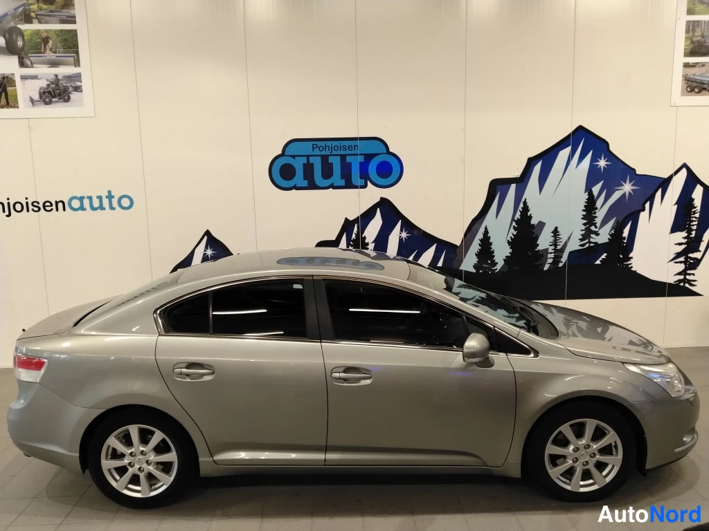 Etuviisto, nokka oikealle: Toyota Avensis -sedan kylki sivusta, hopeisenharmaa kori ja kattoluukku näkyvissä.