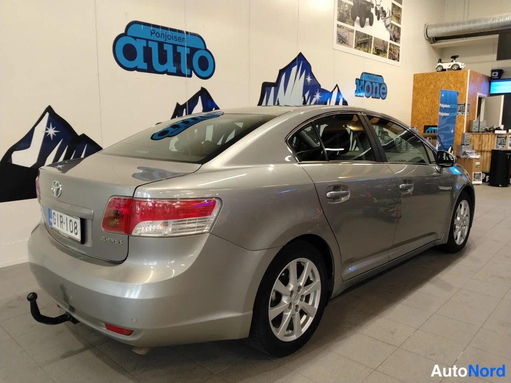 Takaviisto: Toyota Avensis -sedan takaa kulmasta, vasen kylki ja takapää näkyvissä, hopeisenharmaa kori, rekisteritunnus.