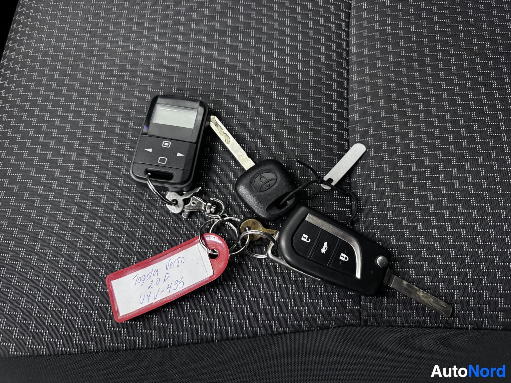 Muu: Avainnipussa kaksi avainta, Toyota-avaimenperä, kauko-ohjain ja punainen kenttä, johon on käsin kirjoitettu 'Toyota Verso 2.0 D '. Taustalla tumma kuviollinen k