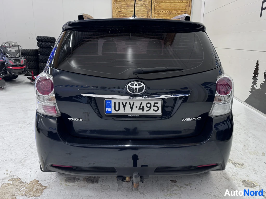 Takaa: Mustan sinertävä Toyota Verso suoraan takaa kuvattuna, rekisterikilpi, vetokoulu näkyvissä.