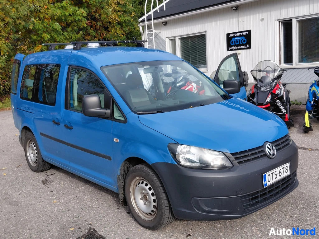 Etuviisto, nokka oikealle: Sininen Volkswagen Caddy -pakettiauto kolmivartaloa, etugrilla ja rekisterikilpi näkyvissä.