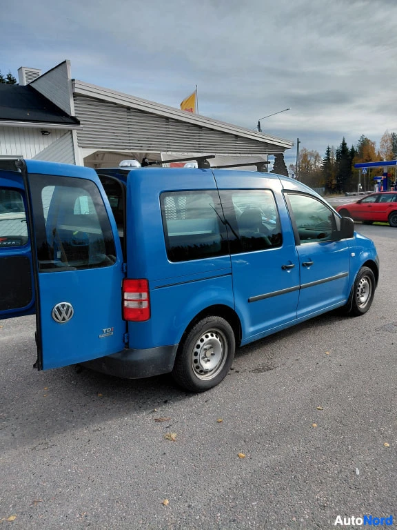 Takaviisto: Sininen Volkswagen Caddy takaviistosta, takaovi auki ja kattoteline asennettuna.