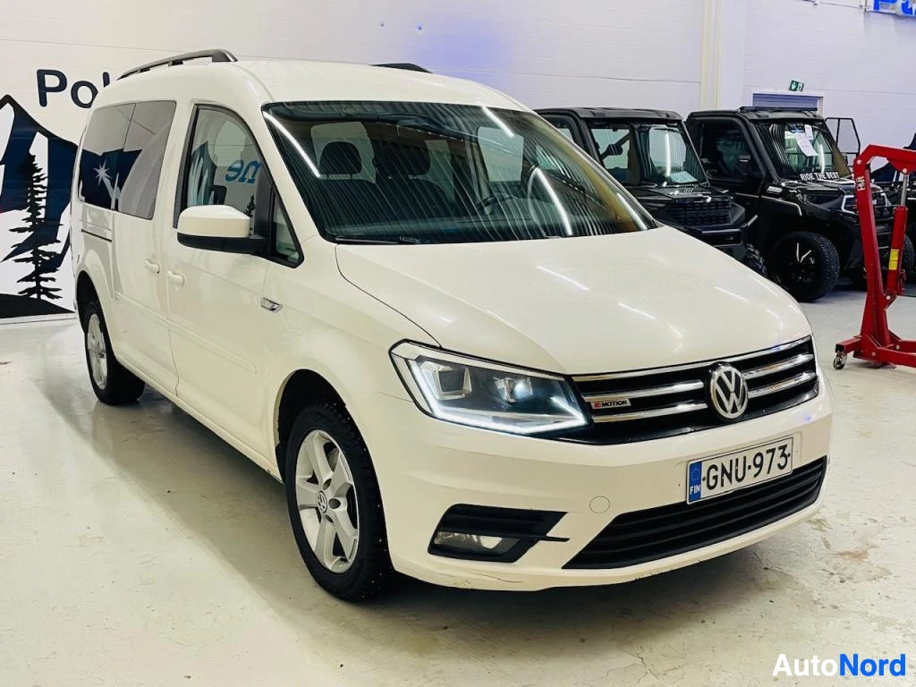 Etuviisto, nokka oikealle: Valkoinen Volkswagen Caddy edestä kolmannelta, rekisteritunnus, kattokaiteet ja kirkas LED-etuvalo näkyvissä.