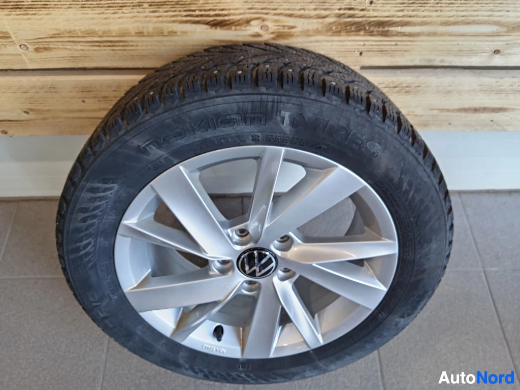 Muu: Nastarenkaalla varustettu hopeinen alumiinvanne, Nokian Tyres -rengas ja Volkswagen-merkki navassa, seisoen lattiaa vasten.