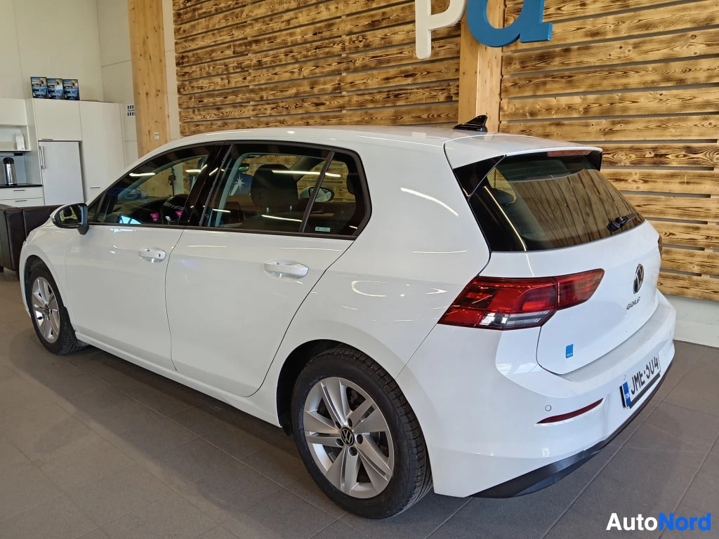 Takaviisto: Valkoinen viisiovinen farmarimallin kori? ei, viisiovinen hatchback taka- ja sivukulmasta: takavalot, VW-merkki ja rekisterikilpi näkyvät, auto sisätiloissa puu