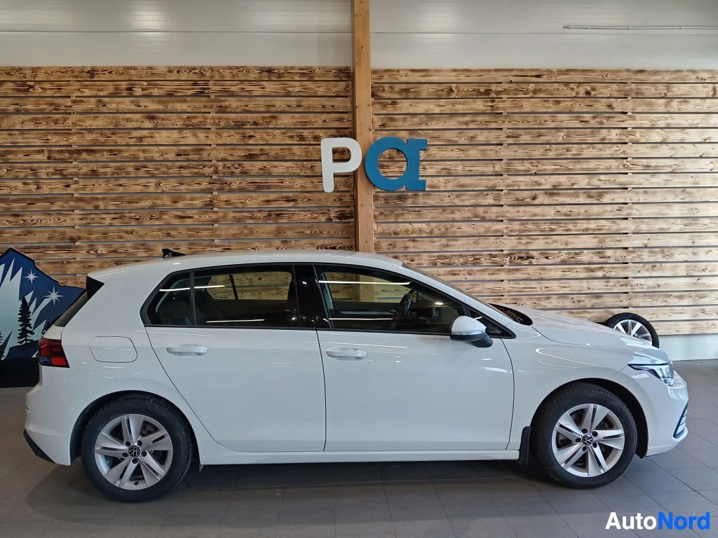Sivulta: Valkean Volkswagen Golfin vasen sivu on tässä kuvassa nähtävissä. Auto seisoo tiloissa, jossa seinässä on puulistoja.