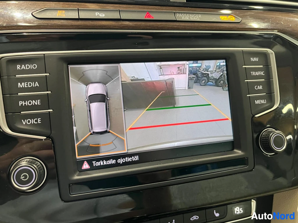 Yksityiskohta: Infotainment-näytöllä takakameran kuva ohjausviivoineen ja ympärinäytön kuvatehoste, tekstillä Tarkkaile ajotietä.