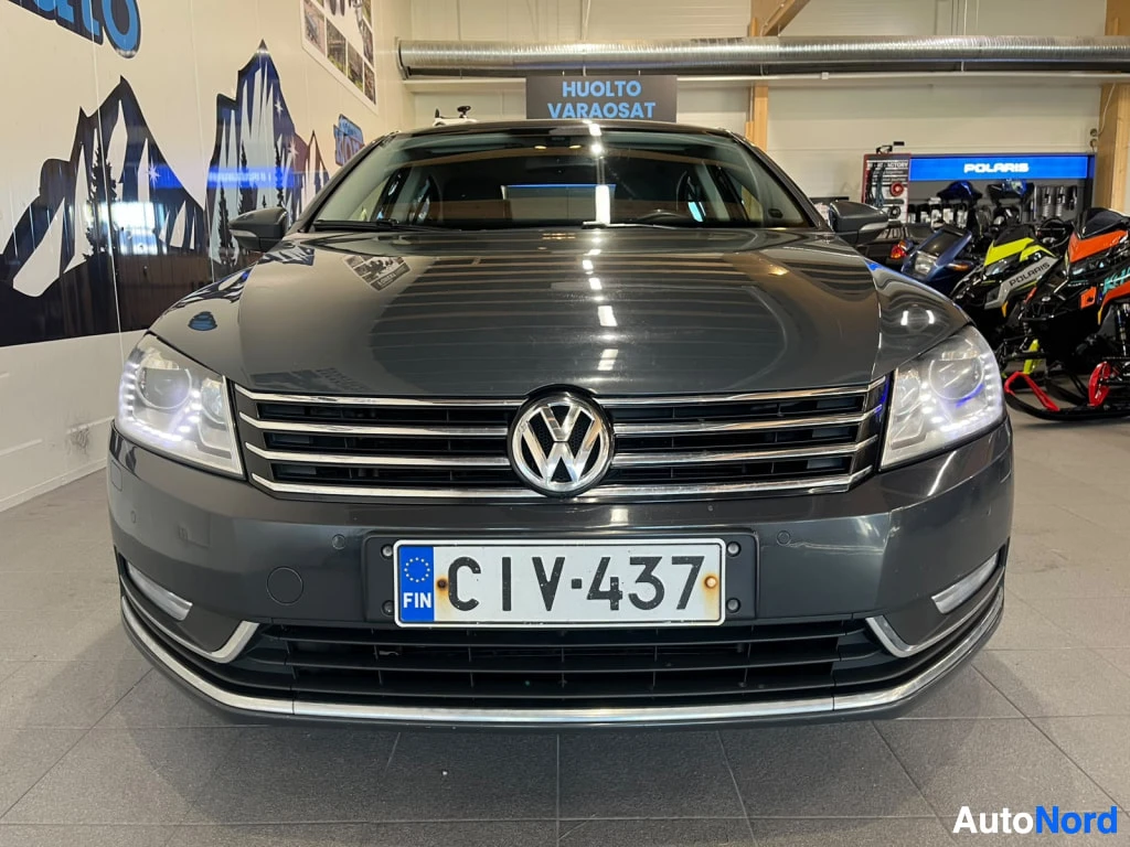 Edestä: Tummanharmaan sedanin etupää suoraan edestä; VW-merkki, kaksoischromauskori ja rekisteri FIN huoltotiloissa.