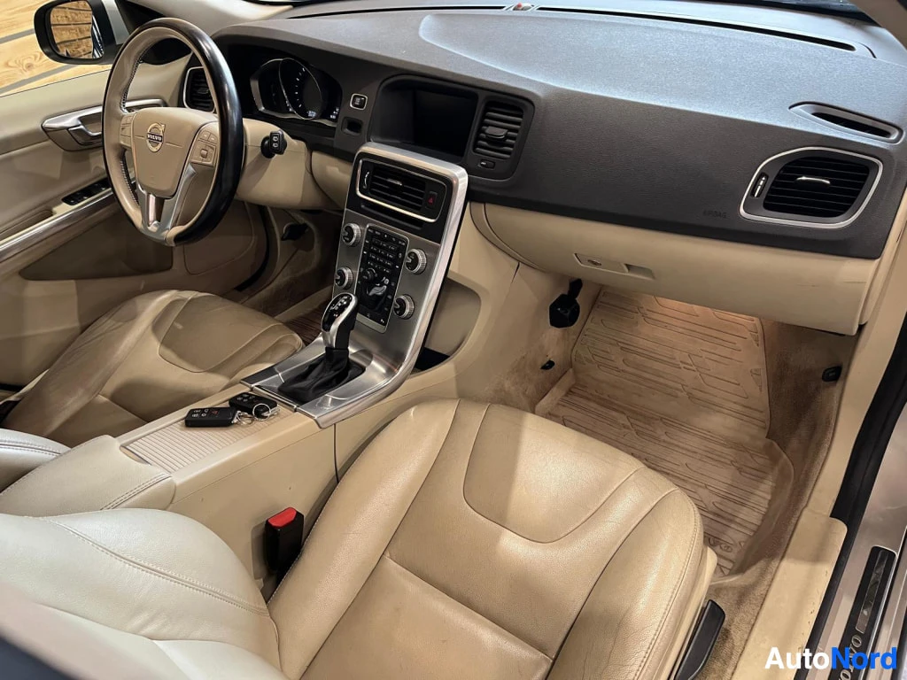 Yksityiskohta: Volvo V60:n etuistuin: beige-nahkainen ohjauspyörä, automaattivaihteen valitsin, radionäppäimet ja beigen matto.