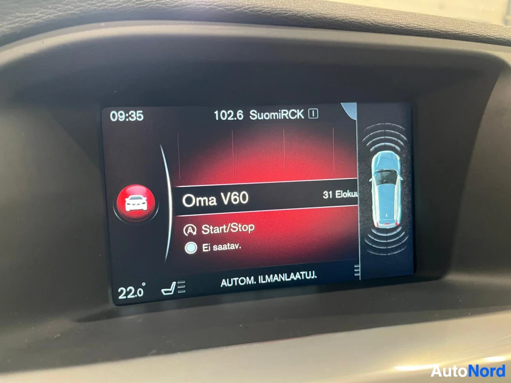 Yksityiskohta: Kojelaudan infotainment-näyttö: radio 102.6 SuomiRCK, valikko 'Oma V60', Start/Stop -toiminto 'Ei saatav.', teksti 'AUTOM. ILMANLAATUJ.', lämpötila 22,0°, sivul