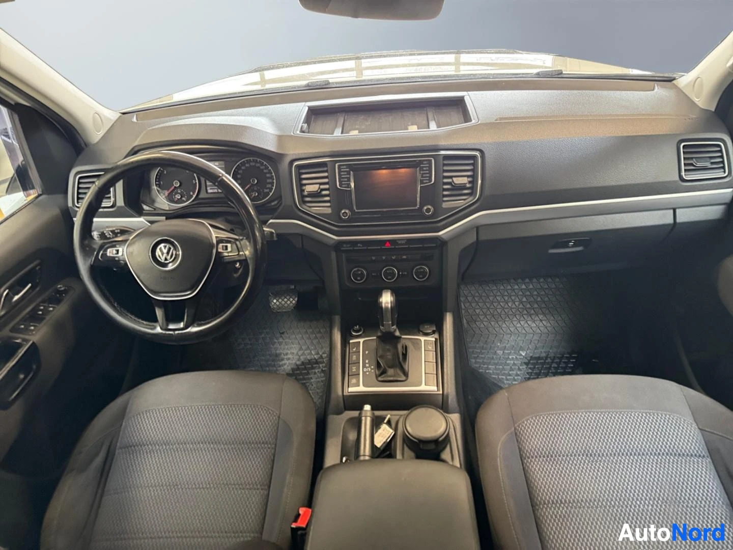 Muu: Kojelaudasta suoraan eteenpäin kuvattu: ohjauspyörä Volkswagen-merkillä, mittaristo, näytöllinen radio ja automaattivaihteen valitsin; kaksi etuistuinta edestä