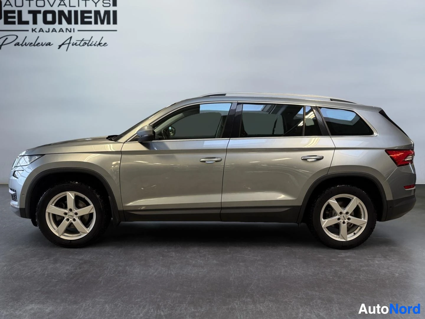 Etuviisto, nokka vasemmalle: Hopeanharmaan Skoda Kodiaq -maasturin sivuprofiili vasemmalta etuviistosta kuvattuna sisätiloissa.