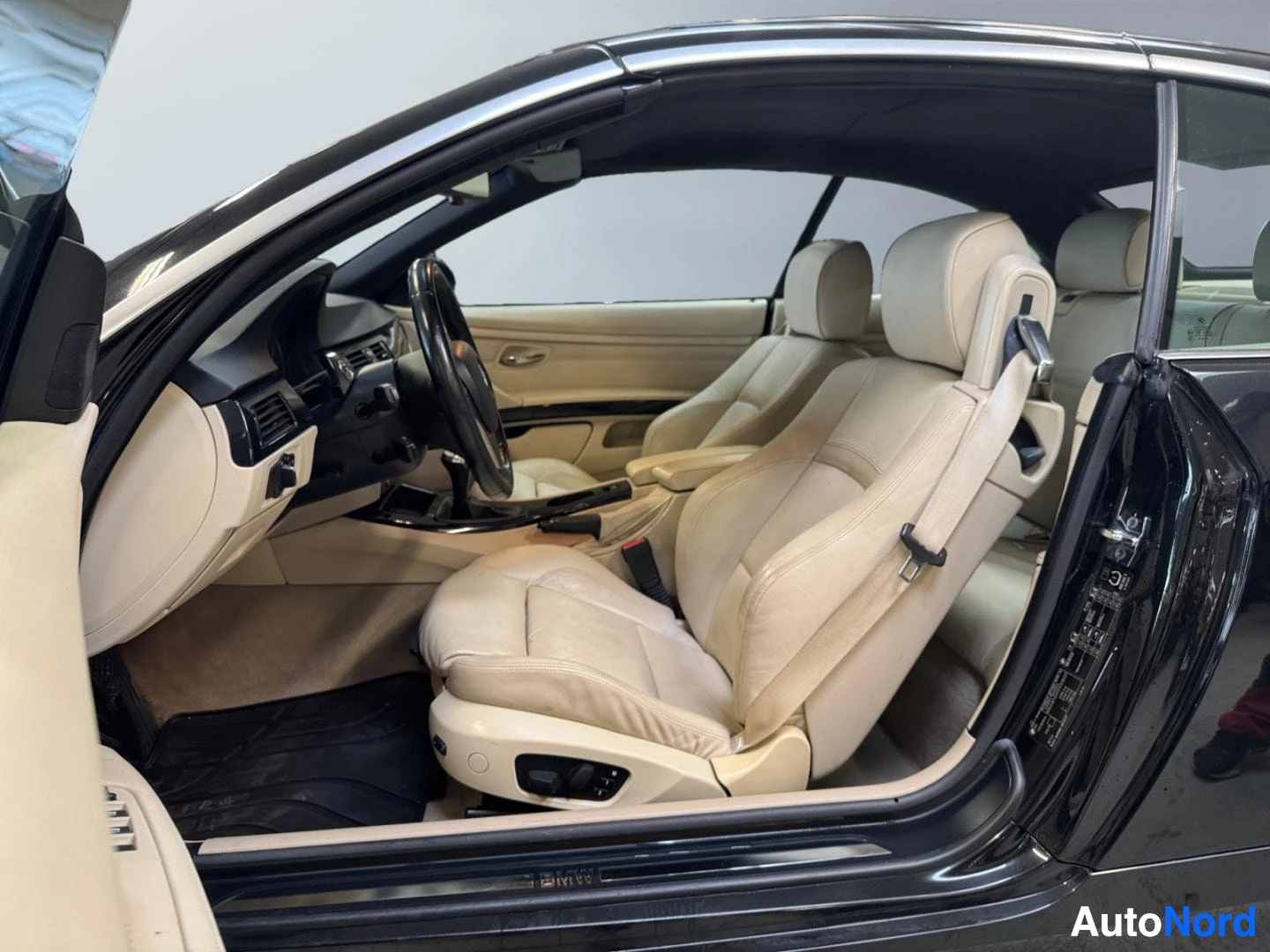 Ohjaamo: Avoauton kuljettajan puolen sisätilat: beige nahkapenkit, ohjauspyörä ja kojetaulu, ovista näkyy BMW-merkki.