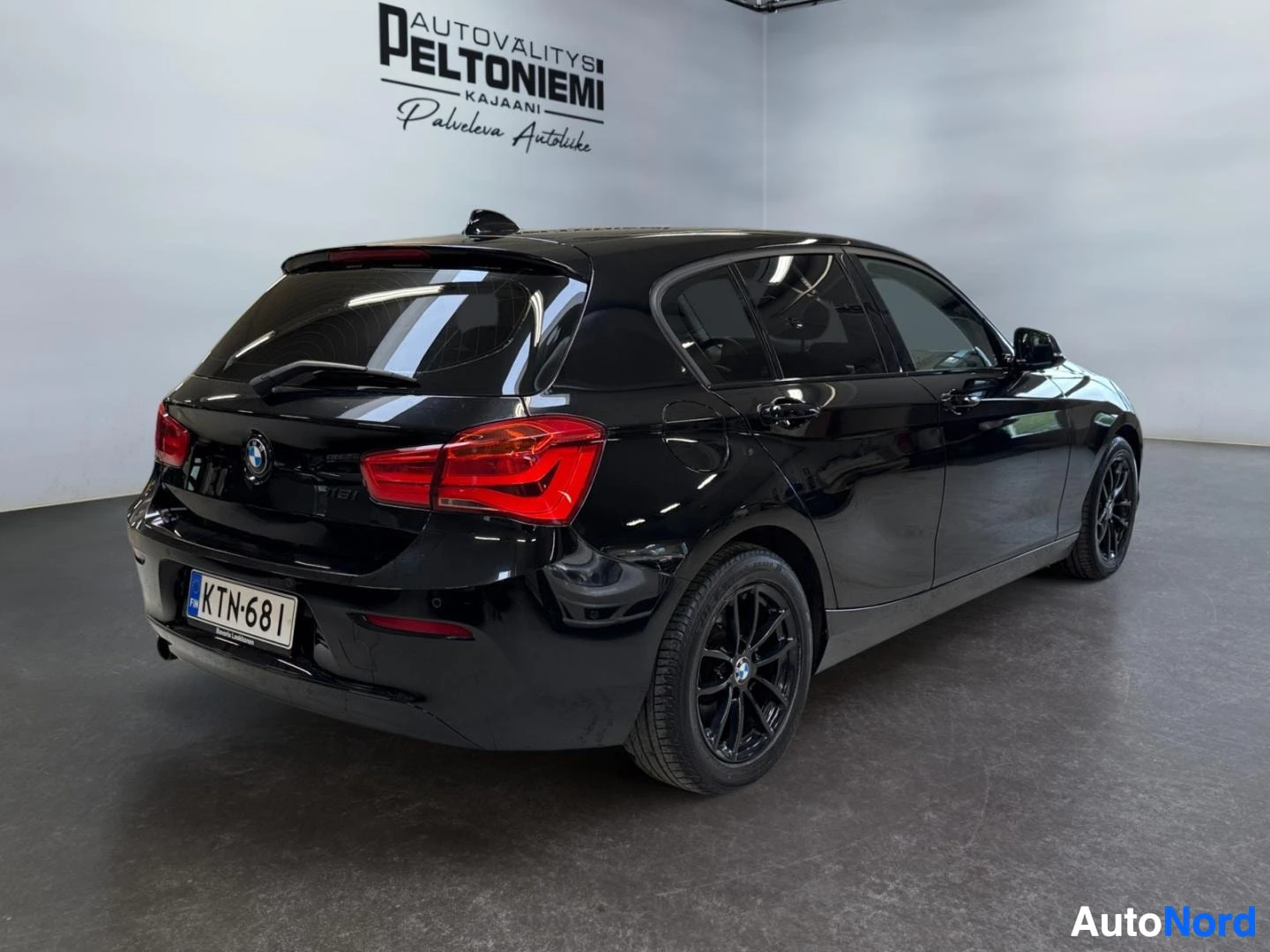 Takaviisto: Musta BMW 1-sarjan viistoperä kuvattu takaa vasemmalta kulmasta, rekisterikilpi, punaiset takavalot.