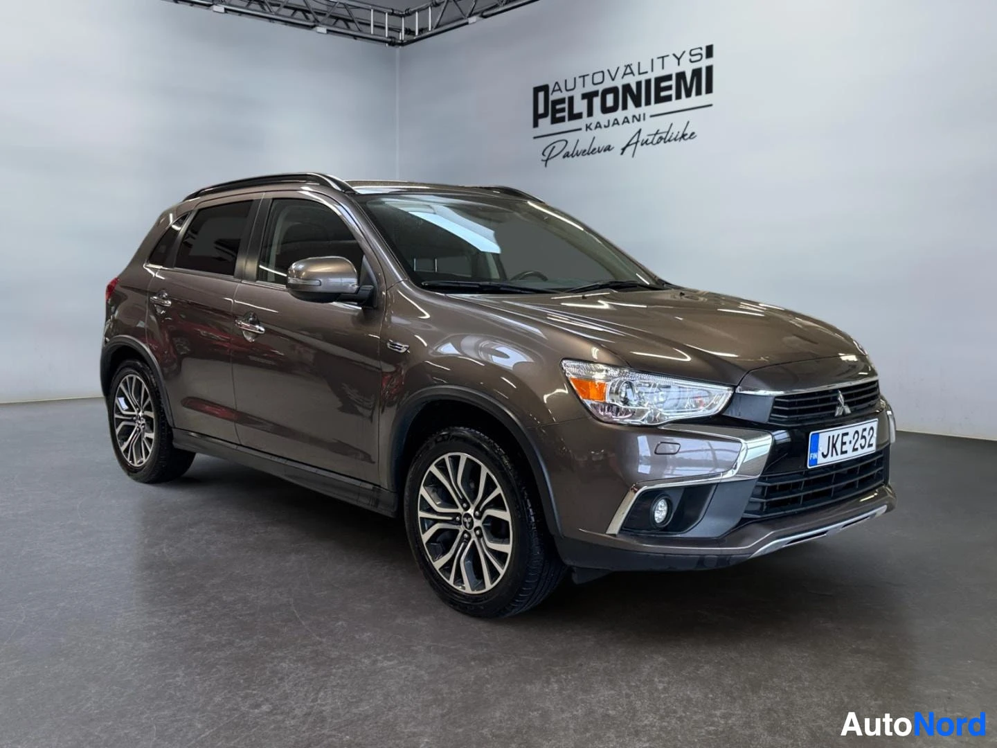 Etuviisto, nokka oikealle: Ruskean metallinhohtoinen Mitsubishi ASX etuviistolta oikealta autonmyymälässä, rekisteritunnus.