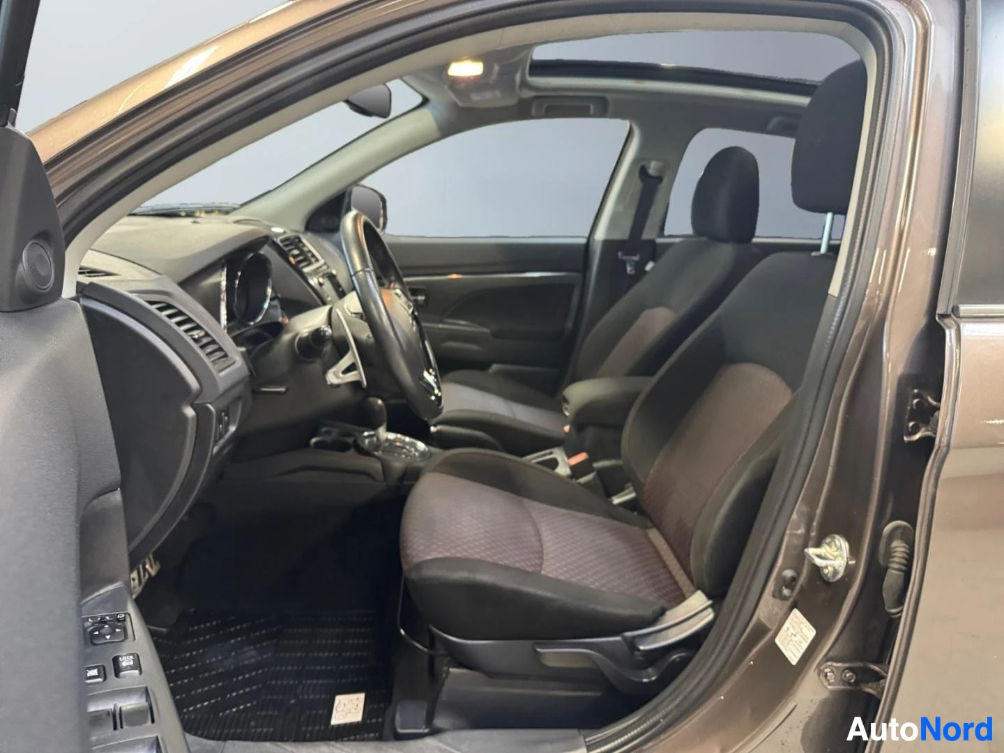 Muu: Mitsubishi ASX:n sisätilat kuljettajan ovesta: tummat kangasistuimet, ohjauspyörä, kojelauta ja aurinkokatto.