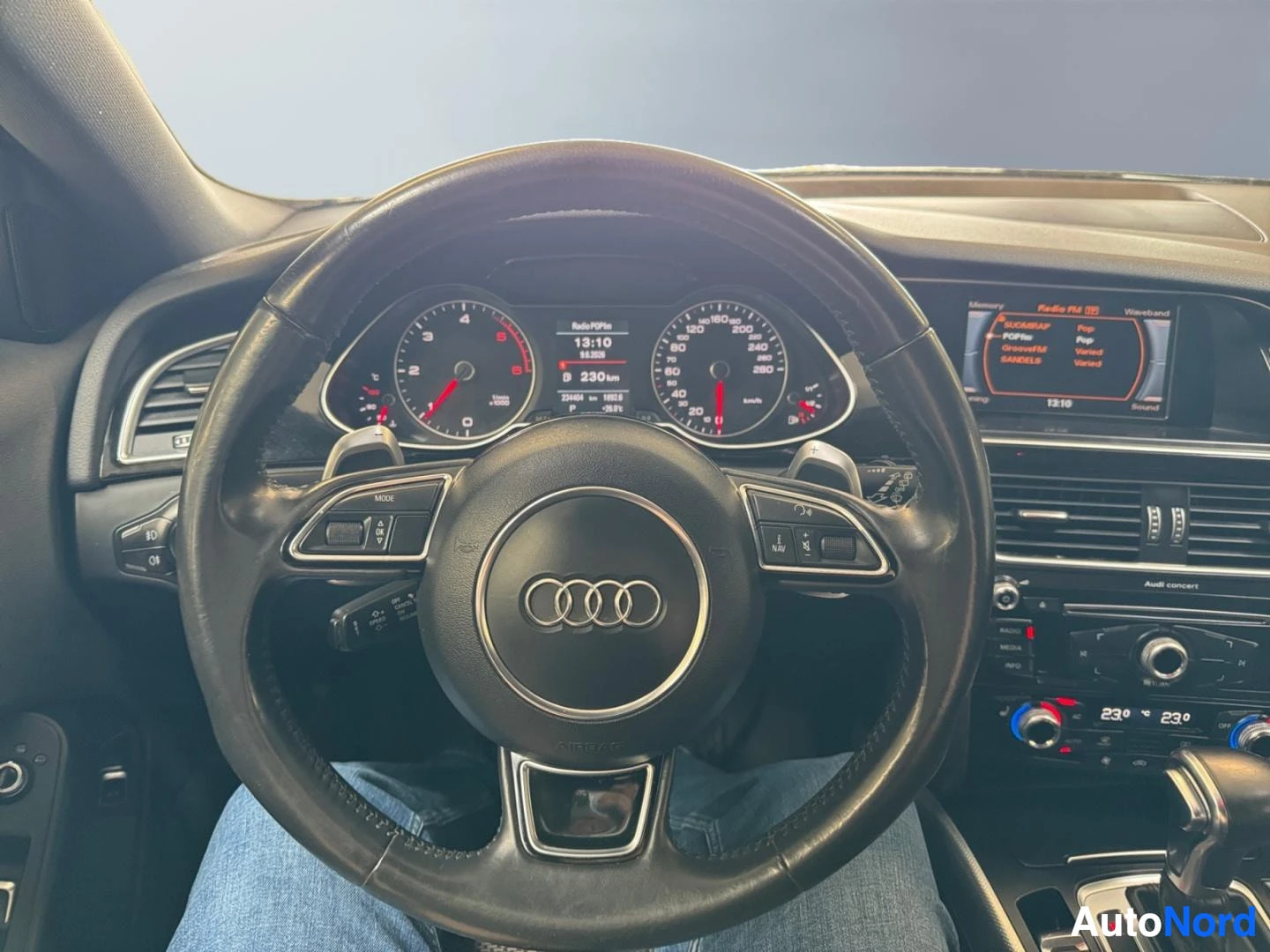 Yksityiskohta: Audi-ohjauspyörä ja mittaristo, joissa näkyy matkatietokoneen lukema 230 km ja radioikkuna.