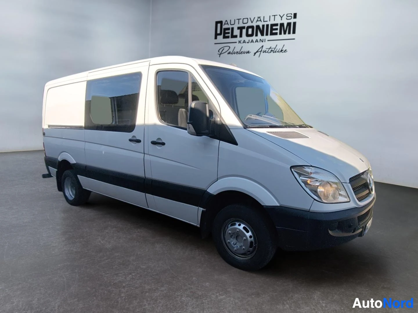 Etuviisto, nokka oikealle: Valkoinen Mercedes-Benz Sprinter -pakettiauto etuviistosta oikealta kuvattuna sisätiloissa.