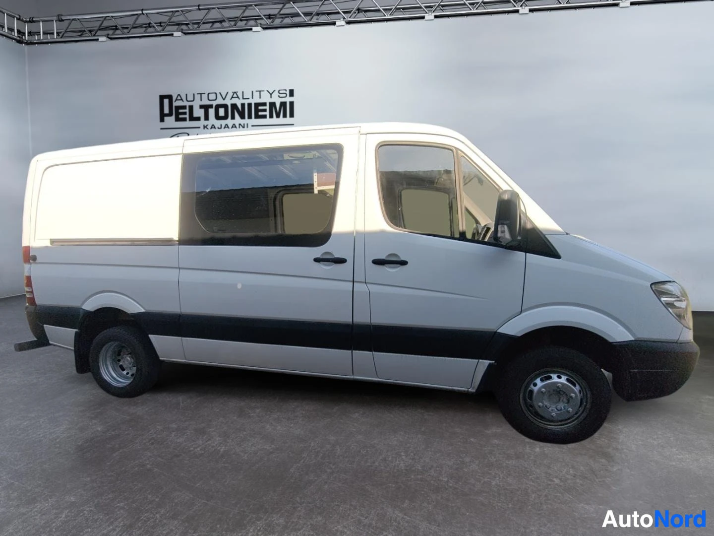 Etuviisto, nokka oikealle: Valkoinen Mercedes-Benz Sprinter -pakettiauto sivultakulmasta oikealta kuvattuna sisätiloissa.